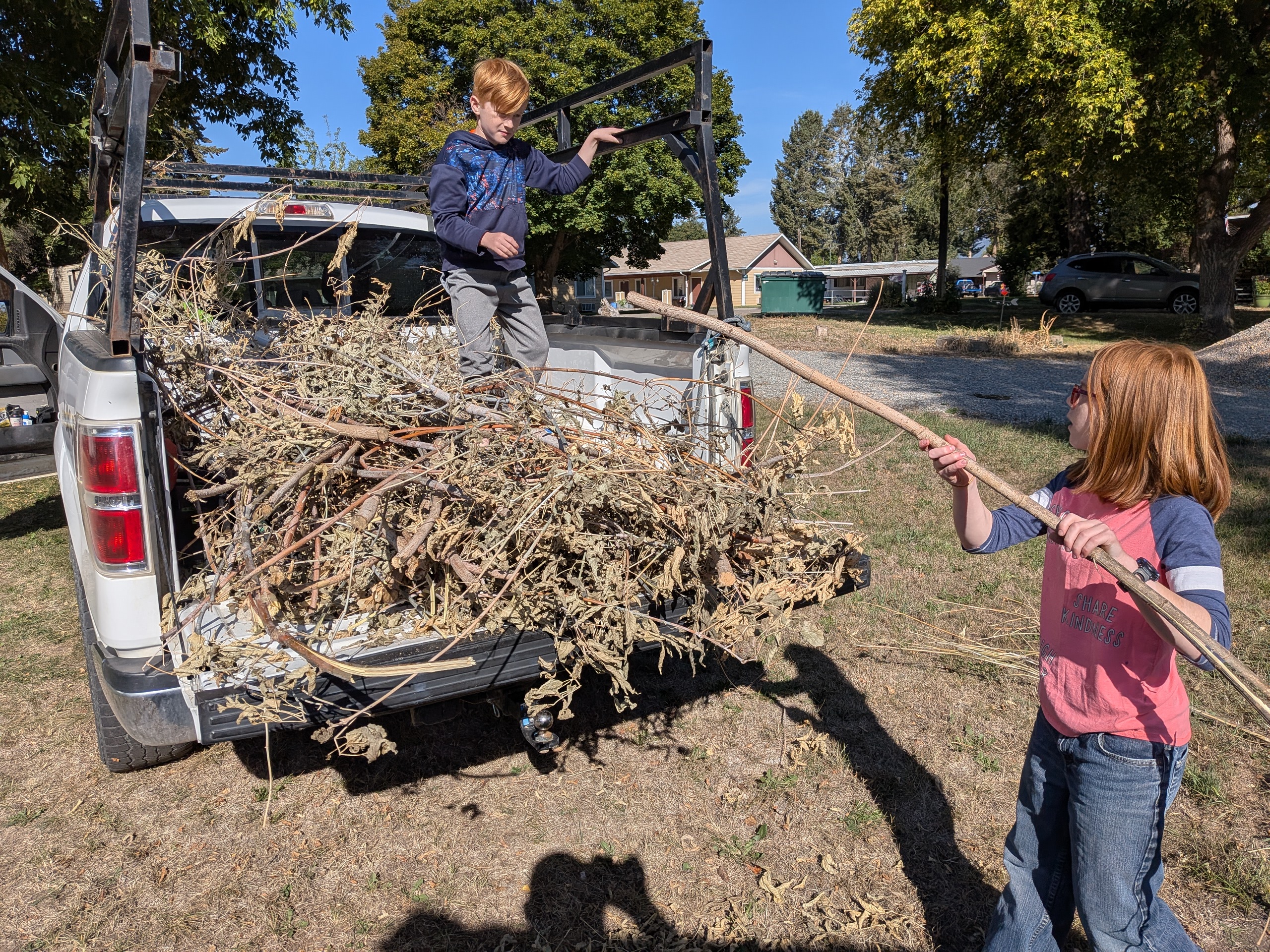 A kid and an adult clearing brush from a roadside ditch with mountains in the distance